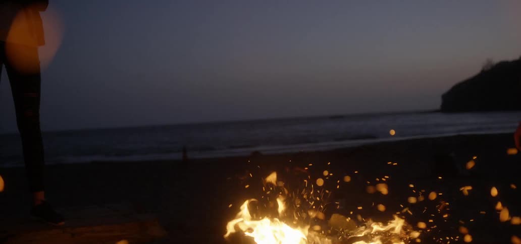 Embers billow from a campfire on the beach