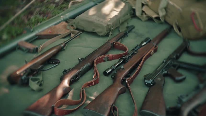 Some rifles with slings on top of a green cloth on the ground