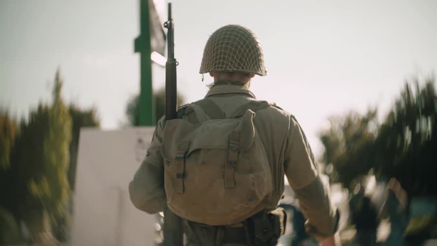 Soldier with backpack and rifle walking through wooded area