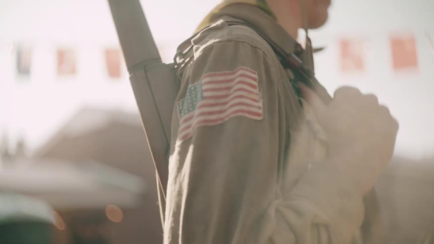 A united states flag on the uniform of a soldier carrying a weapon on his back