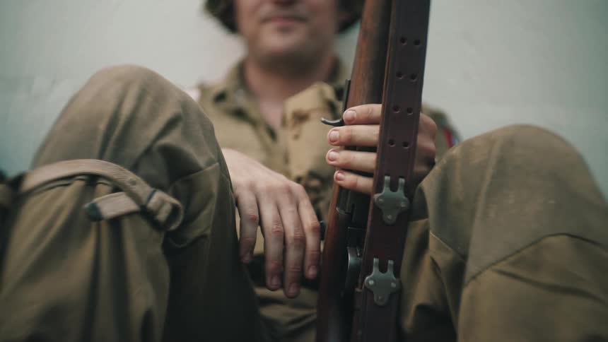 A soldier sitting on the ground holding a weapon with a brown bandolier
