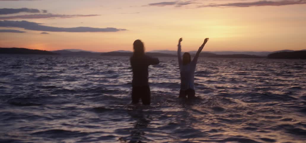 A fully dressed man and woman splash in a lake at sunset