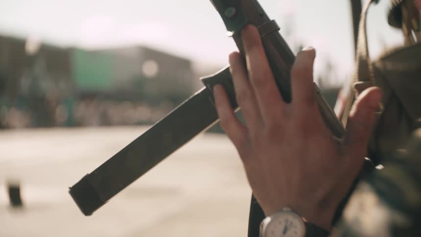 A soldier wearing a helmet and uniform quickly reloads a weapon inserting a straight magazine into the firearms receiver in a bright hazy outdoor setting