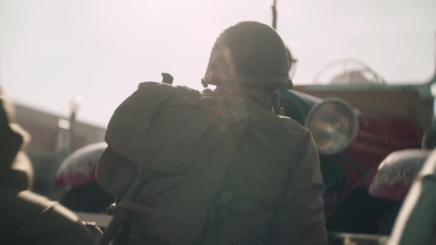 Soldier seen from behind walks toward a military vehicle under strong outdoor light