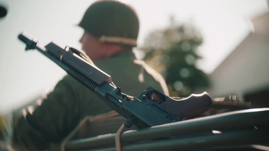Rifle rests on a metal structure with a soldier in the background outdoors