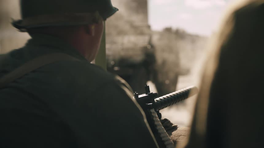 Soldiers observe a military vehicle in motion with dust suspended in the outdoor environment