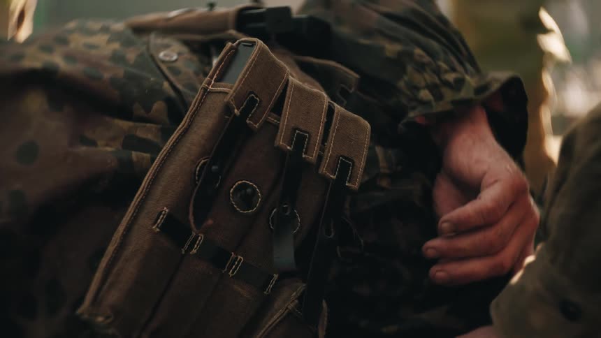 Hand holding the arm of an injured soldier wearing camouflage uniform with visible military gear