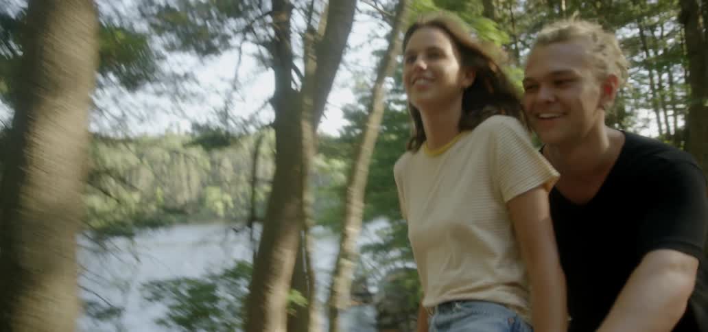 A man and a woman ride a bike together near a body of water with trees