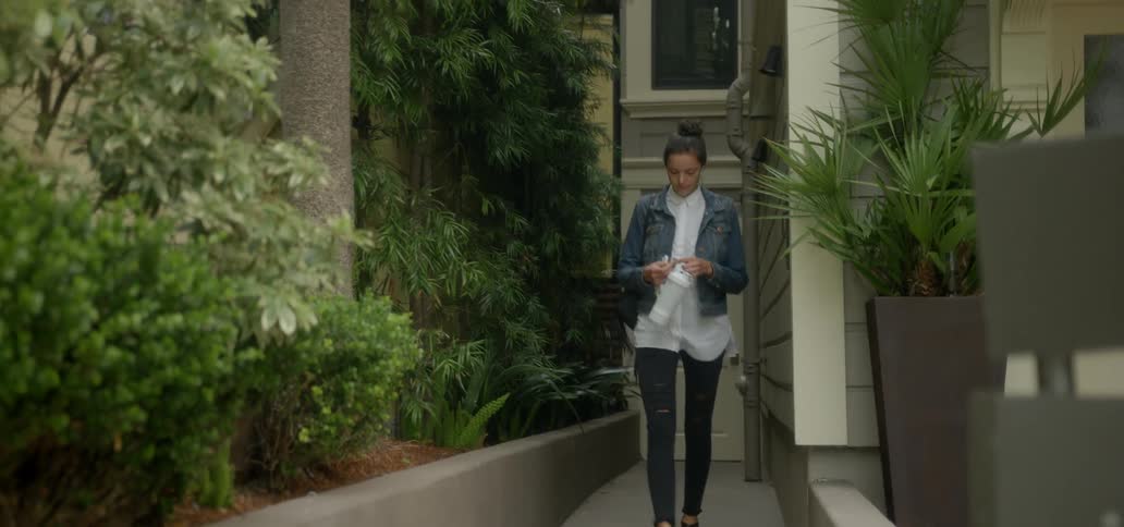 A woman walks outside an apartment building while putting in earbuds