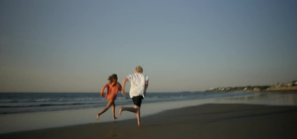 A man and woman run on a sandy beach