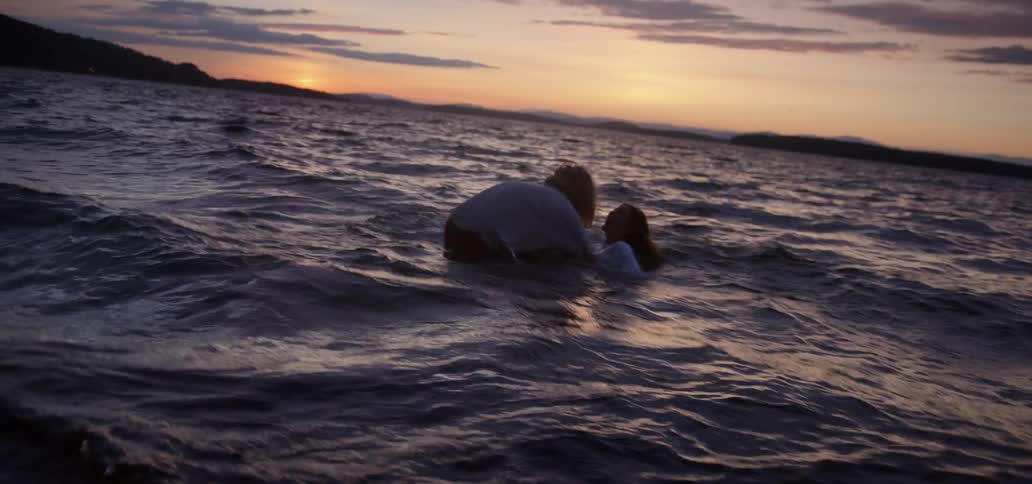 A man and woman play and run in the ocean at sunset