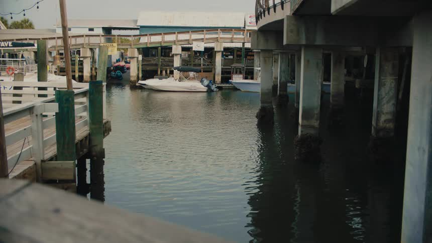 Small boats docked in the marina as a pedestrian walks by buildings along the coast