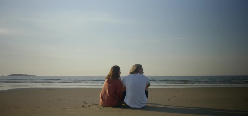 A man and woman sit on a sandy beach