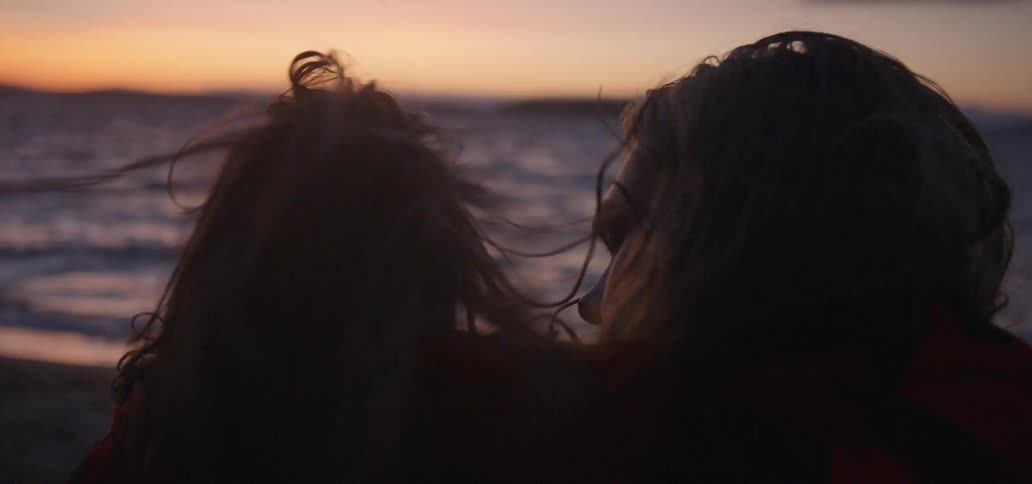 A man and a woman cuddle on the beach during sunset