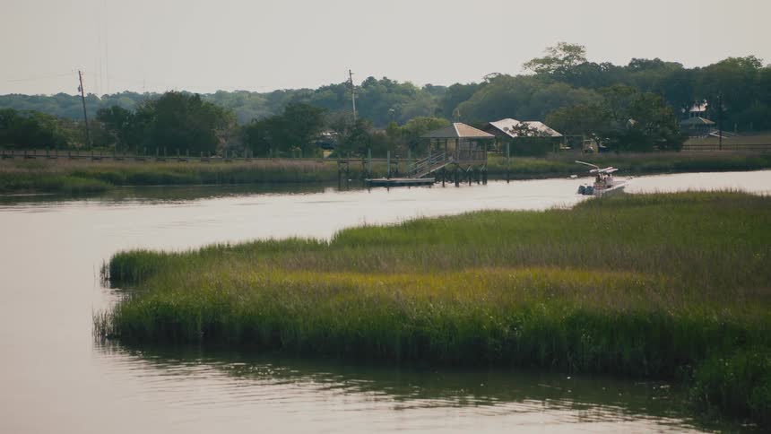 A boat moving along a river at midday with the riverbank lined with open grassland