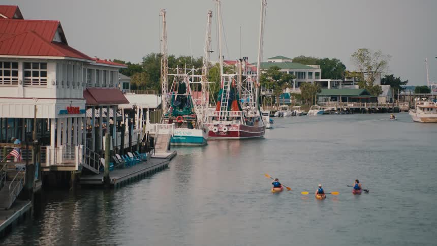 Buildings along the coast as people sail in kayaks on the river