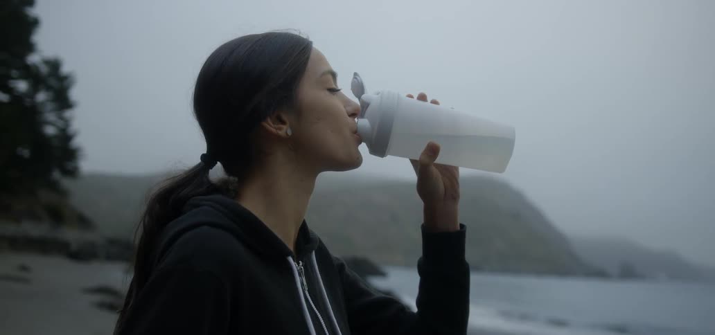 A woman drinks from a water bottle on a beach