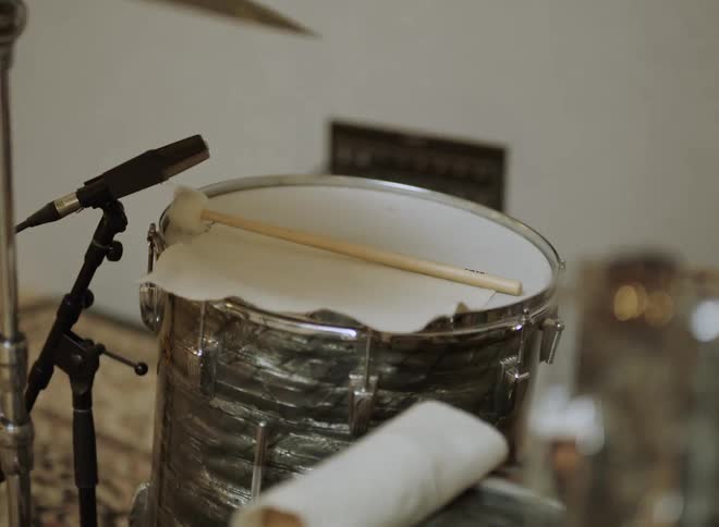 A closeup shot of a pearlwrapped snare drum with a drumstick resting on the head positioned next to a small microphone on a stand in an indoor setting