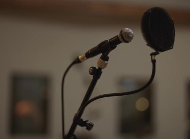 Microphone with pop filter mounted on stand in front of blurred indoor wall