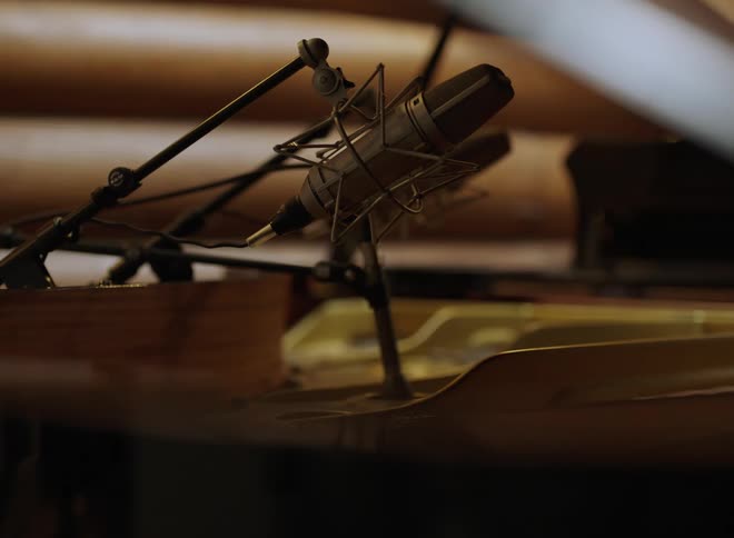 Condenser microphone positioned above grand piano in studio with wooden acoustic panels