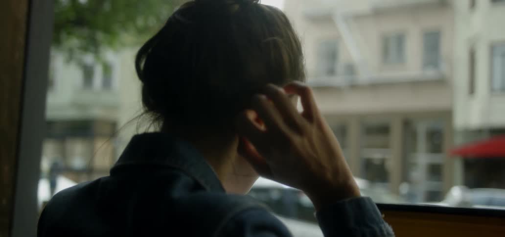 A woman smooths the hair behind her ear on a city sidewalk