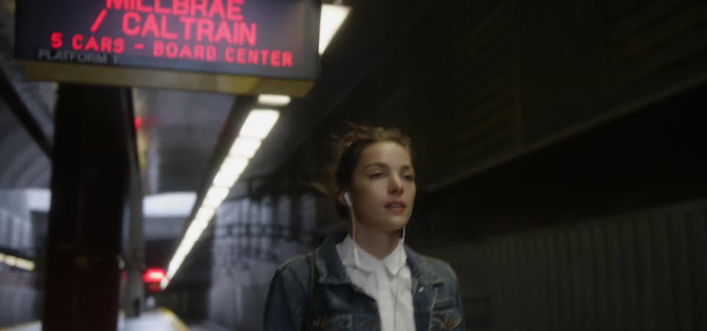A woman wearing ear buds and walking through a subway station