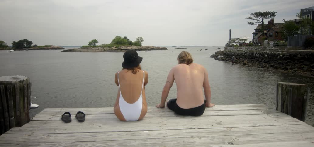 Man and woman sitting at edge of dock overlooking lake on cloudy day