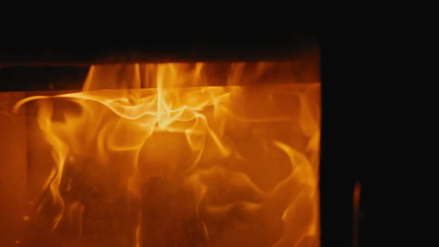 Orange and yellow flames dance brightly over burning wood inside the dark firebox of a stove or fireplace