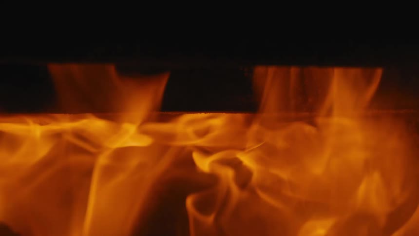 Vivid orange and yellow flames move upward in a slow motion close view inside a dark fireplace or wood burning stove