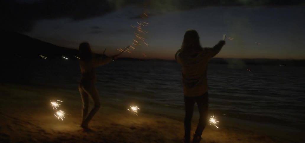 A man and woman shoot fireworks into the sky at night