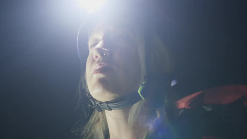 Woman wears a helmet with a headlamp while observing the surroundings in a dark environment