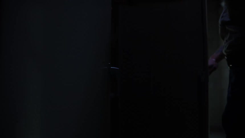 A person opens a door revealing another door marked exit as bright light streams into the dark room then closes the door again returning the room to darkness