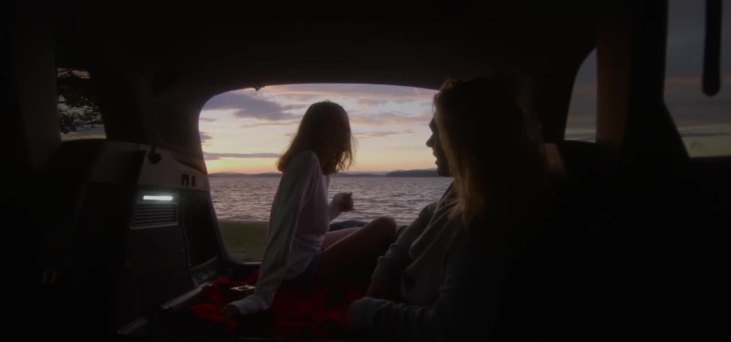 Man and woman sit inside a vehicle next to a body of water