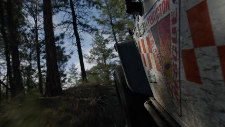 A race car driving through the woods at midday its body splashed and streaked with puddle water