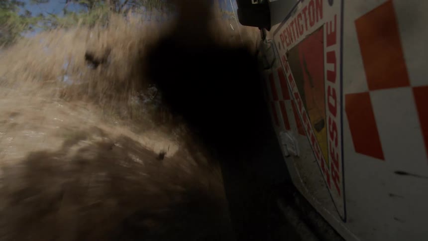 The side of a penticton search rescue truck splashes mud and water as it quickly drives through a deep puddle on a dirt forest road