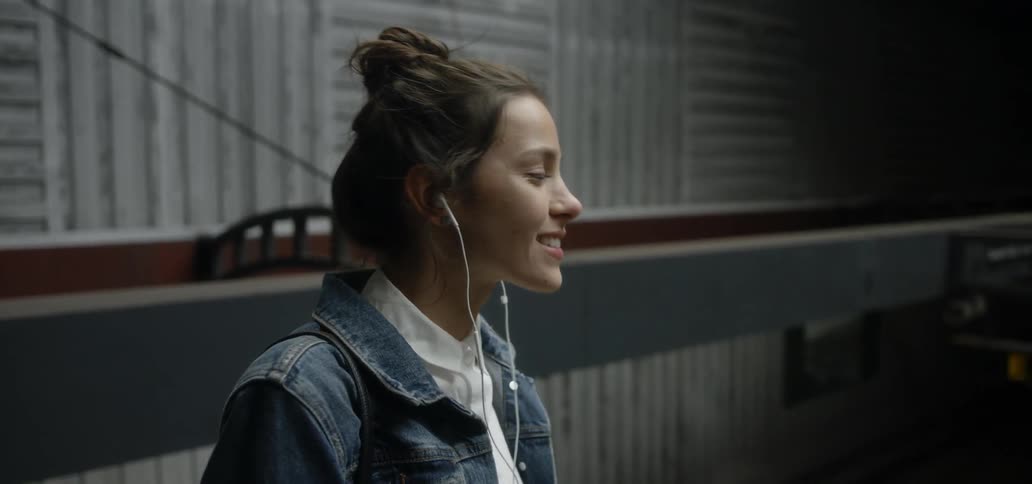 A woman uses earbuds while riding on an escalator