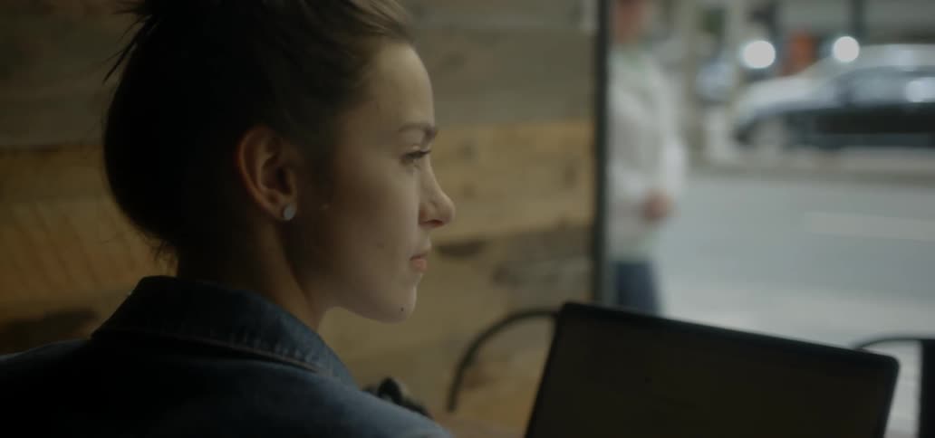 A woman sits in front of a laptop by a cafe window