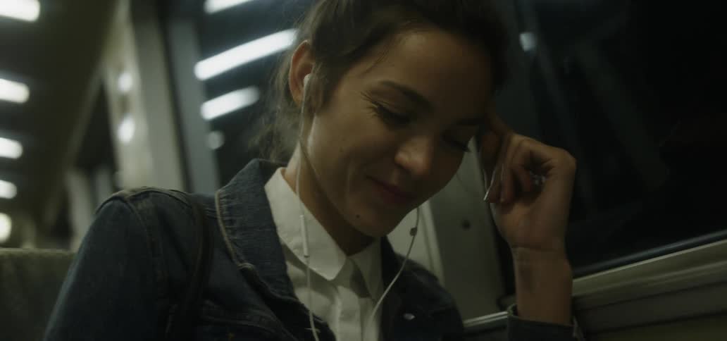 Girl wearing headphones riding on a bus at night is smiling