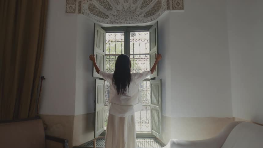 The woman opens the shutters on the window