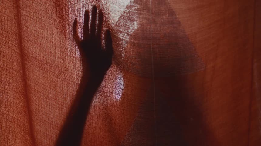 Shadow of a hand appears behind a lit translucent curtain