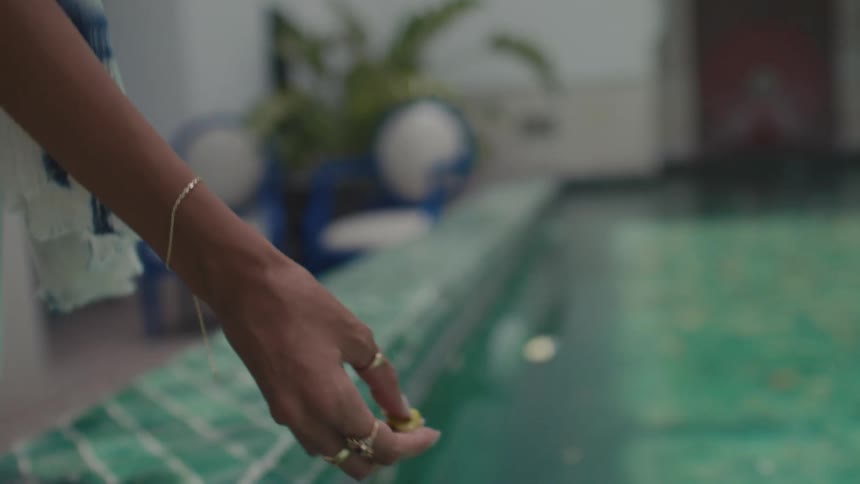 Hand with rings approaches the surface of the water leaving a petal in the pool