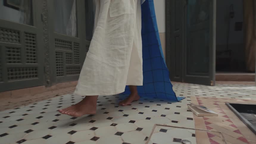 Person walking barefoot on geometric floor with trailing blue checkered fabric in indoor setting