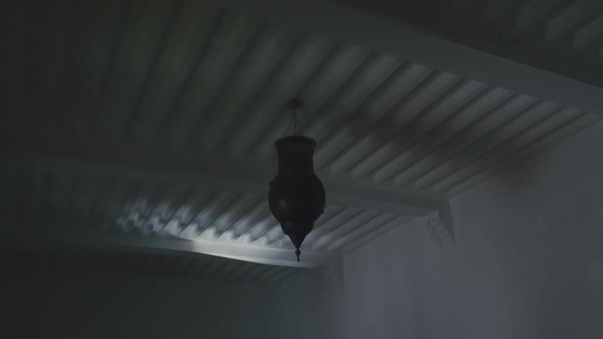 Ornate hanging lantern on white ceiling with exposed beams in dark and moody setting