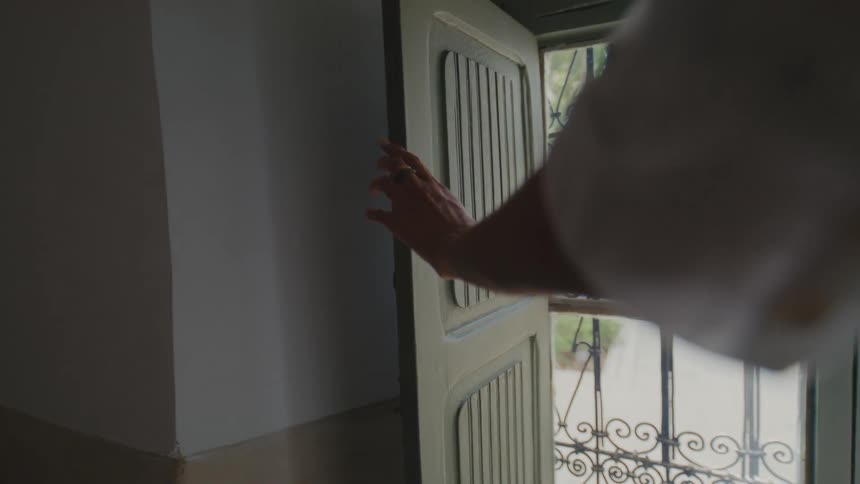 Hand pushes a partially open door with a view of an exterior metal grille