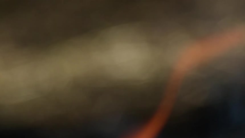 An out of focus abstract view shows warm orange firelight and dark earth with smoke or steam drifting upwards