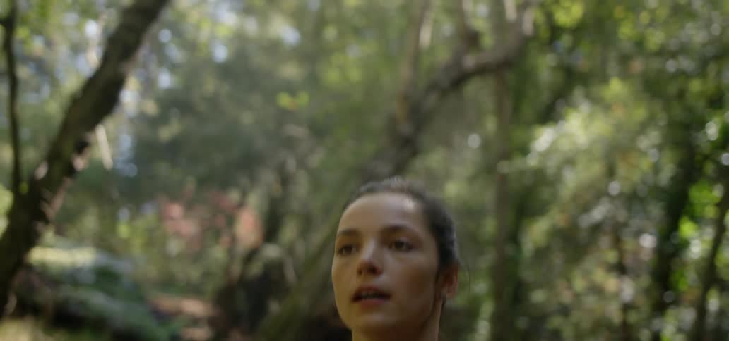 A woman jogs beneath trees on a sunny day