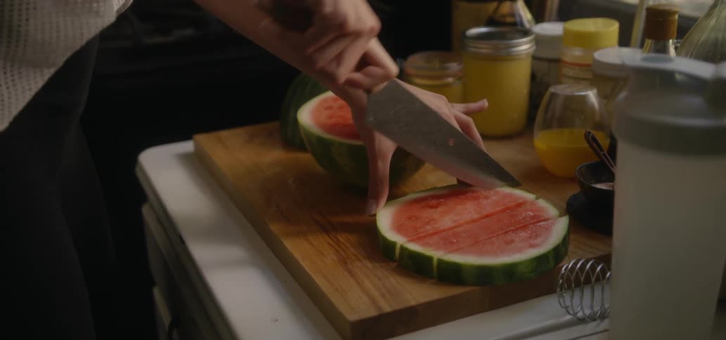 A person in a kitchen slicing a watermelon