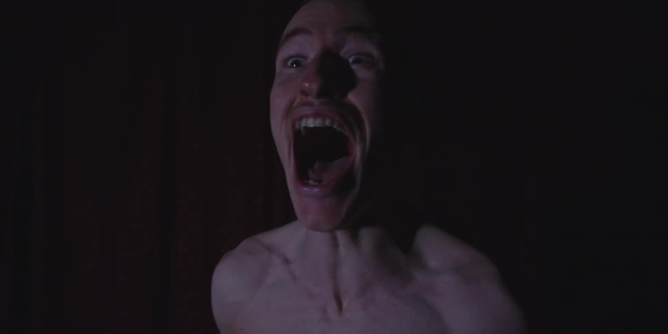Man with mouth open in a scream under low lighting and a dark background