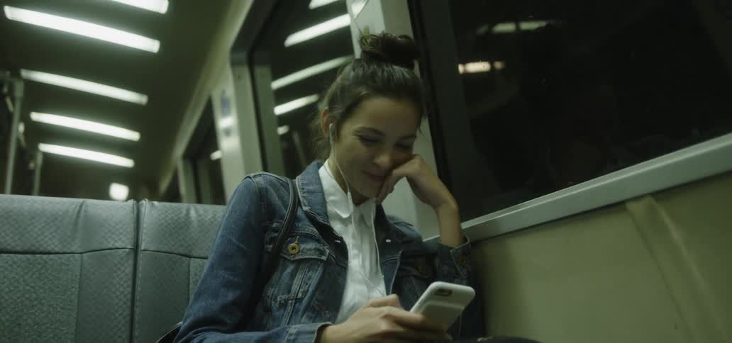 A girl wears headphones and smiles on the bus