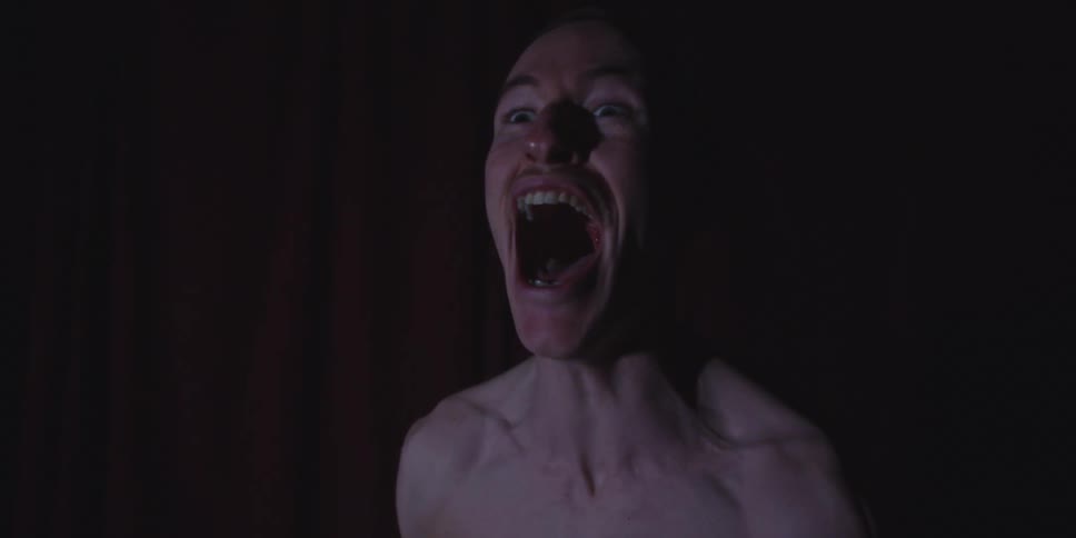 Person screams with mouth open in a dark setting